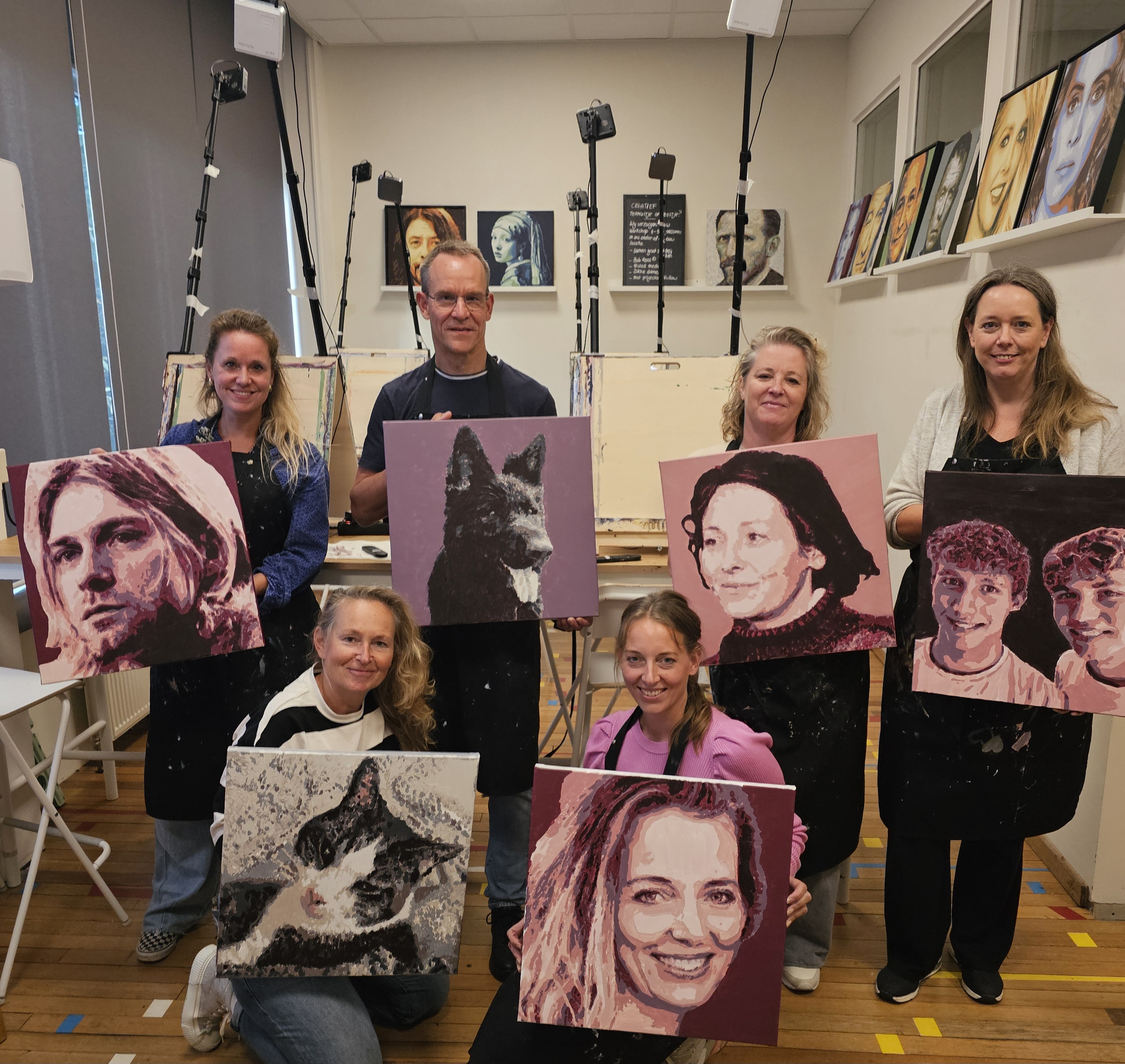 Groep deelnemers in het atelier die hun zelfgemaakte portretschilderijen omhooghoudt