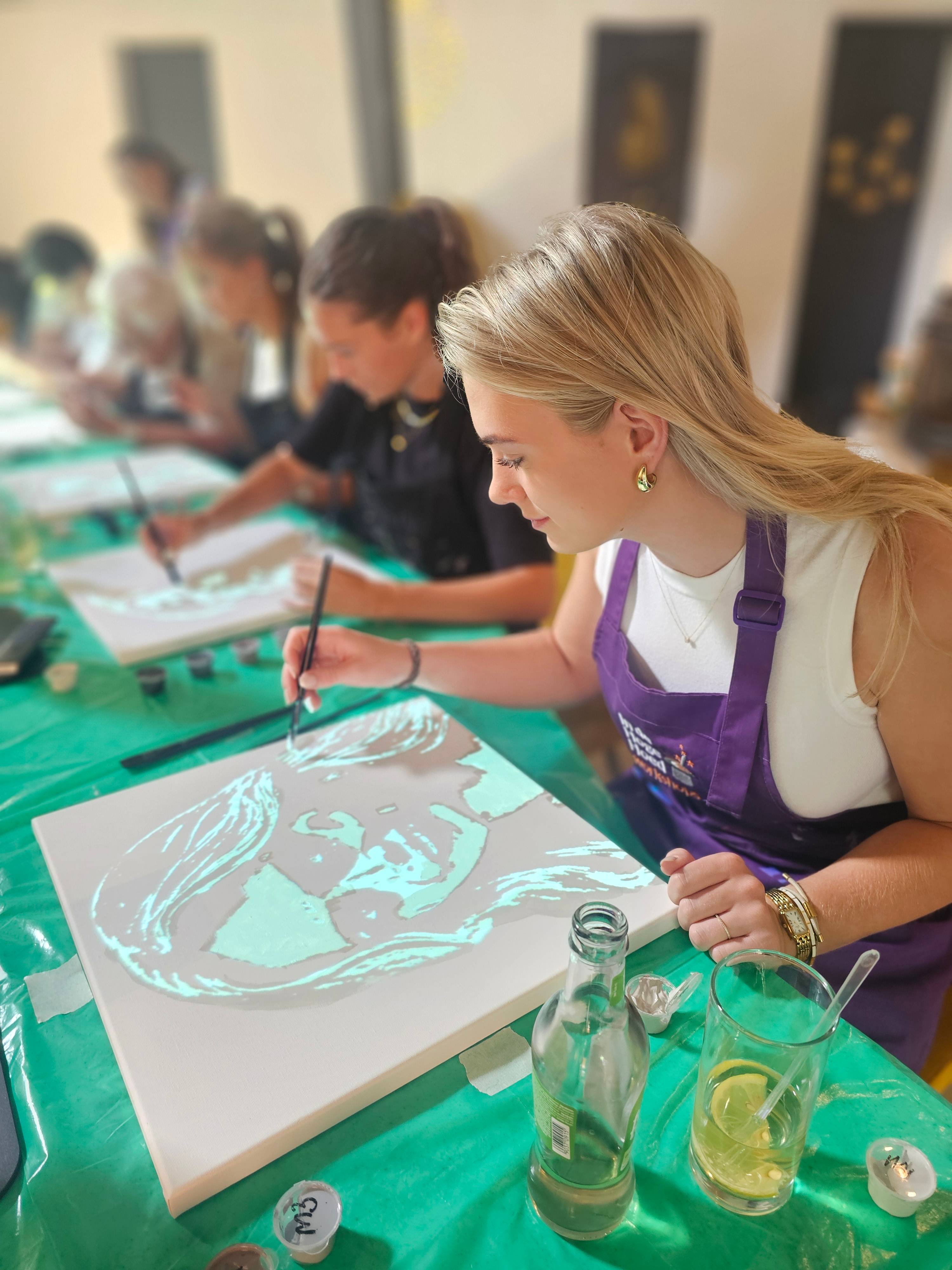 Deelnemer in paars schort schildert met een penseel een geprojecteerd portret op canvas tijdens een workshop