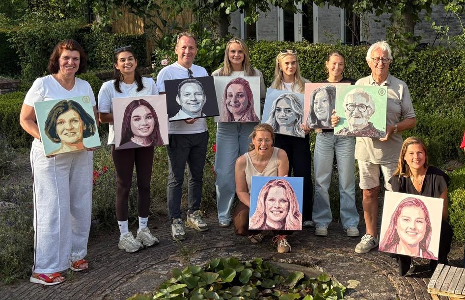 Groep deelnemers in de tuin die lachend de zelfgemaakte portretten uit de workshop van In de Hoge Hoed omhooghoudt